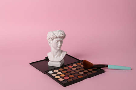 Antique David bust with makeup eyeshadow palette on pink background. Minimal beauty still life.の写真素材