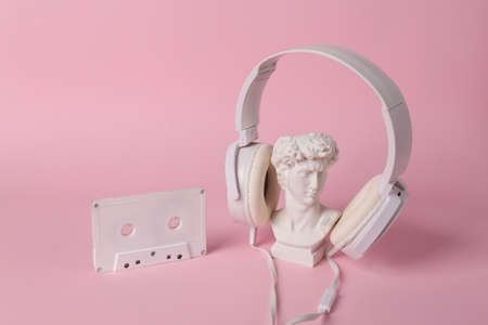 Antique bust of David with headphones and audio cassette on pink background. concept pop. Minimal still life. creative music layoutの写真素材