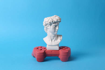 Antique David bust with gamepad on blue background. Gaming. concept pop. Minimal still life.