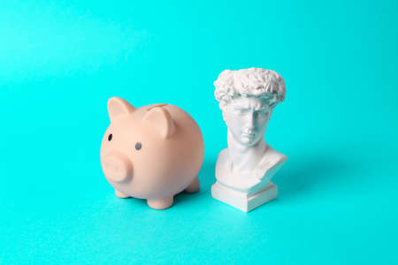 Antique bust of David with piggy bank on turquoise background. concept pop. Minimal still life.の写真素材