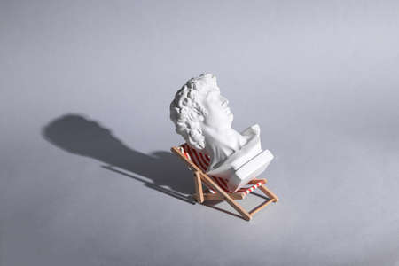 Perfect vacation concept. Bust of David rests on beach deck chair. gray background. Minimal still...