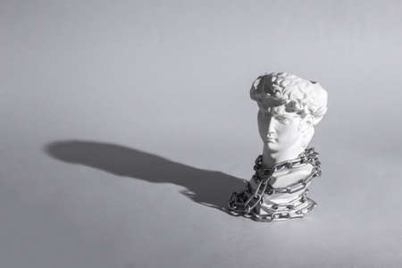 Antique bust of David wrapped steel chain on gray background. concept pop. Minimal still life....