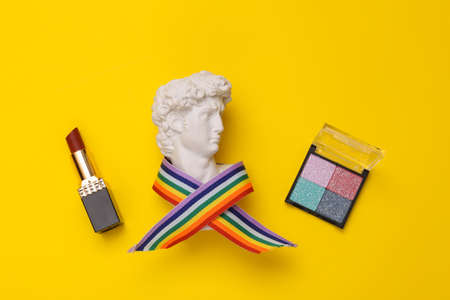 David Bust in rainbow tape with lipstick and eye shadow palette on yellow background. Minimal beauty still life. flat layの写真素材
