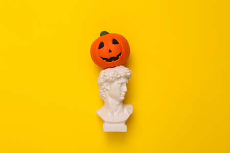 Plaster bust of David with jack lantern pumpkin head on yellow background. Halloween concept. Minimal still life photoの写真素材