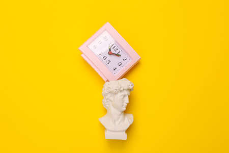 Antique David bust with clock on yellow background. concept pop. Minimal still life. creative ideas. flat layの写真素材