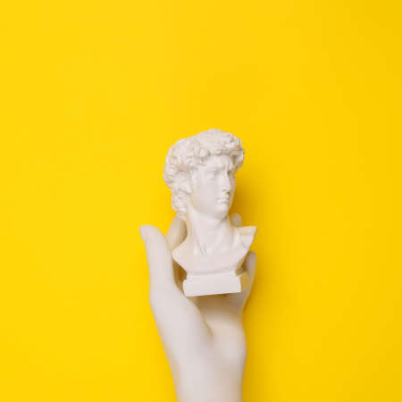 Hand holding David bust on yellow background. Minimal still life