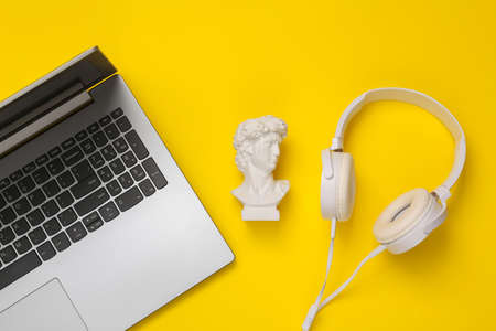 Antique bust of David with headphones and laptop on yellow background. concept pop. Minimal still life. creative layout. top viewの写真素材