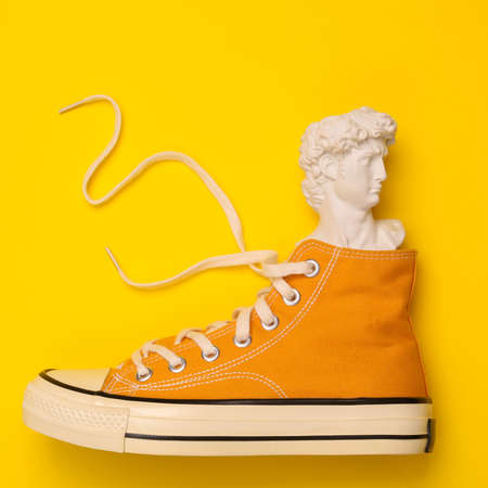 Minimal still life. Antique David bust in sneakers on yellow background. top viewの写真素材