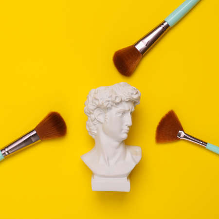 David Bust with makeup brushes on yellow background. Minimal beauty still life. flat layの写真素材