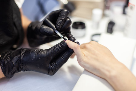 Manicurist paints with nail polish the nails of a woman's clint in nail salon. The working processの写真素材