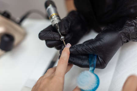 Manicure master removes cuticles with electric file machine on female hand in nail salonの写真素材