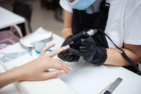 Manicure master removes cuticles with electric file machine on female hand in nail salonの写真素材