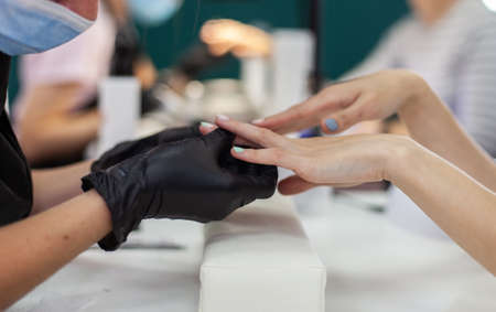 Manicurist in black gloves holds the hands of a woman client and examines the done manicureの写真素材