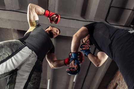 Two sparring partners of a kickboxer in boxing gloves practice kicks in a sports hallの写真素材