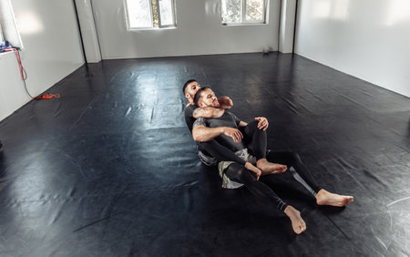 Two athletic male fighters are training, practicing a painful hold in a sports hall.の写真素材