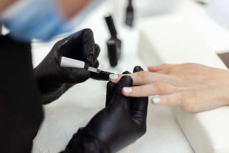 Manicurist paints with nail polish the nails of a woman's clint in nail salon. The working processの写真素材