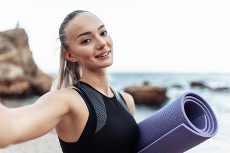Selfie portrait of smiling fit woman in sport wear with yoga at on wild beachの写真素材
