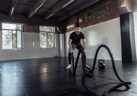 Male athlete trains with battle ropes in a sports hall