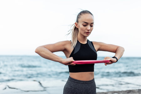 Young beautiful fit woman in sportwear training with a fitness elastic band (expander) on a urban...