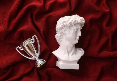 David plaster bust with winner cup on red crumpled silk background