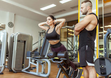 Young fit woman training muscles with personal trainer man in the gym
