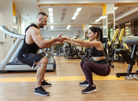 Athletic man with woman squats holding hands in the gym. Workout togetherの写真素材