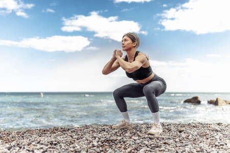 Athletic muscular woman in sportswear trains leg muscles on the beach. bodybuilding and fitness. outdoor workoutの写真素材