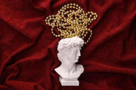 David plaster bust with Christmas garlands on red crumpled silk background