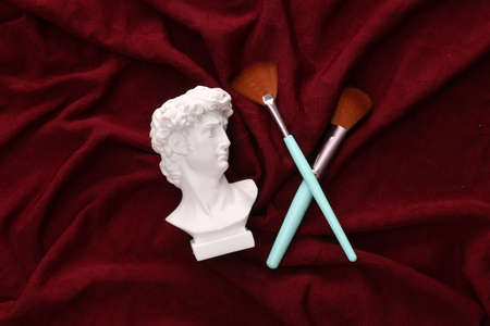 David plaster bust with makeup brushes on red crumpled silk background