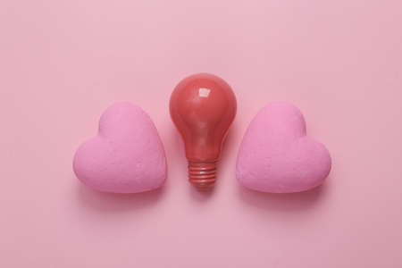 Light bulb and hearts on pink background. love concept. top view