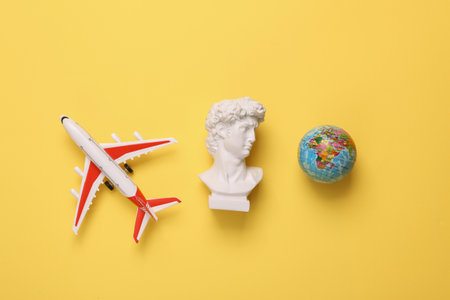 Model airplane and David bust with globe on yellow background. travel concept. Flat lay, top viewの写真素材