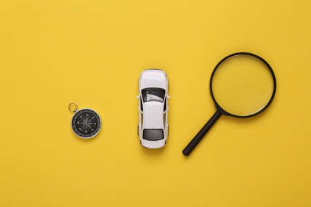 travel concept. Toy car with compass and magnifying glasses on a yellow background. top viewの写真素材