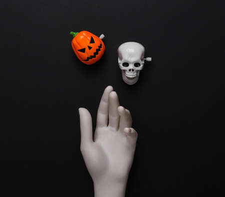 White hand with skeleton head and jack pumpkin on black background. Minimal halloween layout. top...