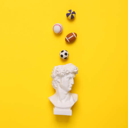 Minimalist still life. Pop concept. David bust with balls of different sports on a yellow background.の写真素材