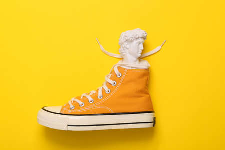 Minimalistic still life. 80s. Pop concept. Bust of David in yellow sneakers on yellow background.の写真素材