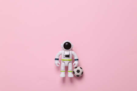 Toy astronaut with a soccer ball on pink background. sports conceptの写真素材