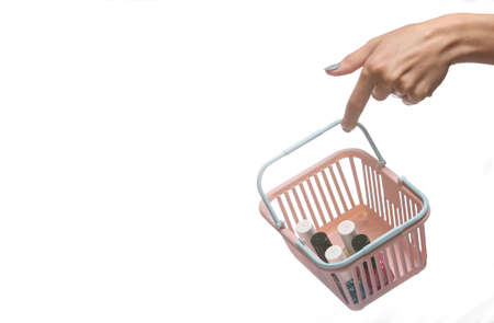 Female hand holding mini shopping basket with nail polish bottles isolated on white background.の写真素材