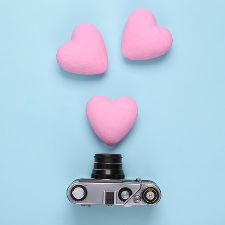Retro camera with hearts on blue pastel background. top view