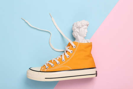 Minimalistic still life. 80s. Pop concept. Bust of David in yellow sneakers on pink blue background.の写真素材