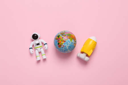 Astronaut toy model with space shuttle and globe on pink background. space mission. flat lay