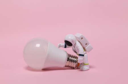 Astronaut in a spacesuit figurine with a light bulb on pink background.