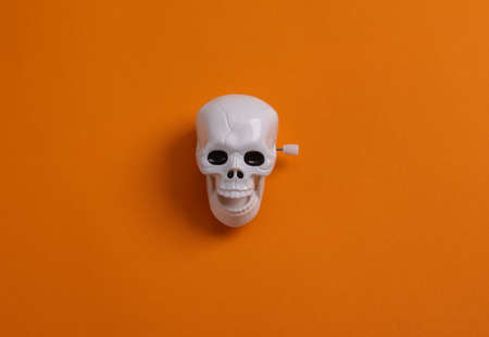Minimal halloween still life. Clockwork skeleton skull on orange background. top viewの写真素材
