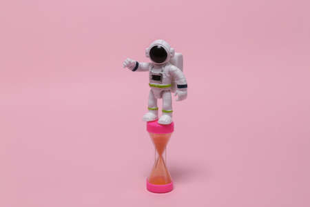 Space mission concept or startup. Astronaut in a spacesuit figurine with hourglass on pink...