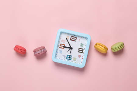 Minimal food still life. Alarm clock with French macaroons on a pink pastel background. creative ideas. flat layの写真素材