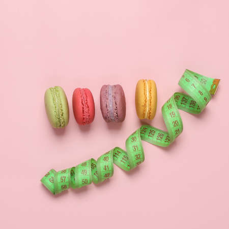 Diet, weight loss concept. Measuring tape with high-calorie french macaroons on a pink background....