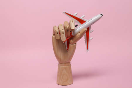 Travel, voyage concept. Model of passenger plane in wooden hand on pink backgroundの写真素材