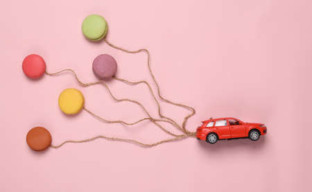 Dreaming, food concept. Car with balloons from French macaroons on a pink background. flat layの写真素材