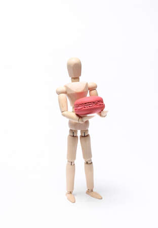 Wooden puppet holding french macaroon isolated on white backgroundの写真素材