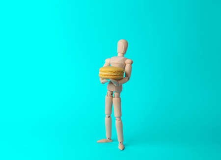 Wooden puppet holding french macaroon isolated on blue background. food conceptの写真素材