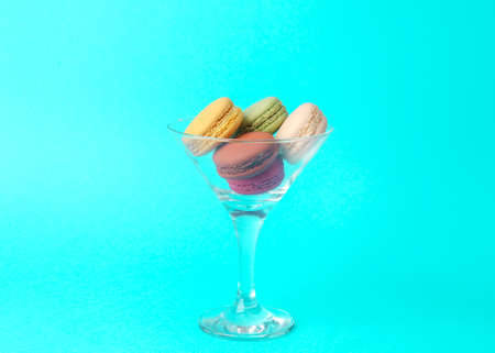 Minimal food still life. Cocktail glass with French macaroons on blue background.の写真素材